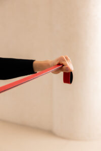 Close-up of a hand gripping a red strap or resistance band stretched horizontally against a beige background.