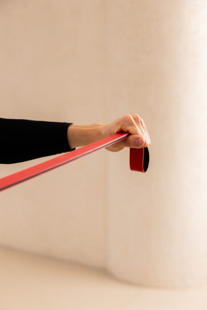 Close-up of a hand gripping a red resistance band stretched across a beige background.