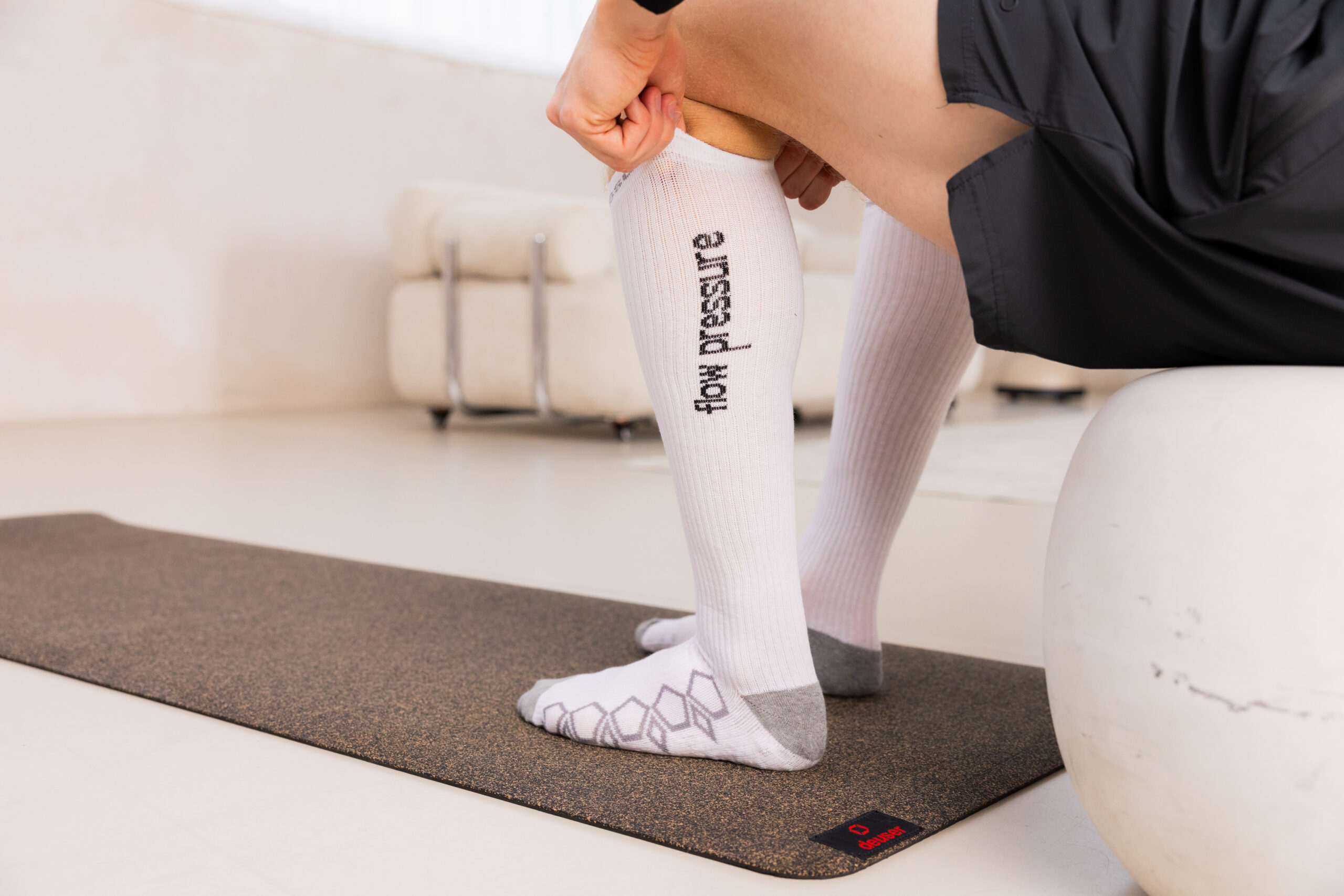 251122_DEUSER-37 - Deuser Sports | Solingen Person kneeling on a dark exercise mat, wearing white knee-high socks with the words 'for progress' running vertically along the leg.