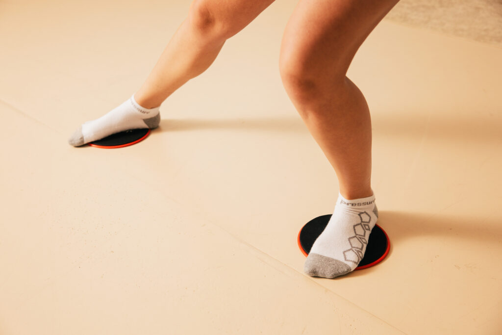 Person balancing on red circular discs with white socks, knees bent, on a light floor (fitness balance exercise)